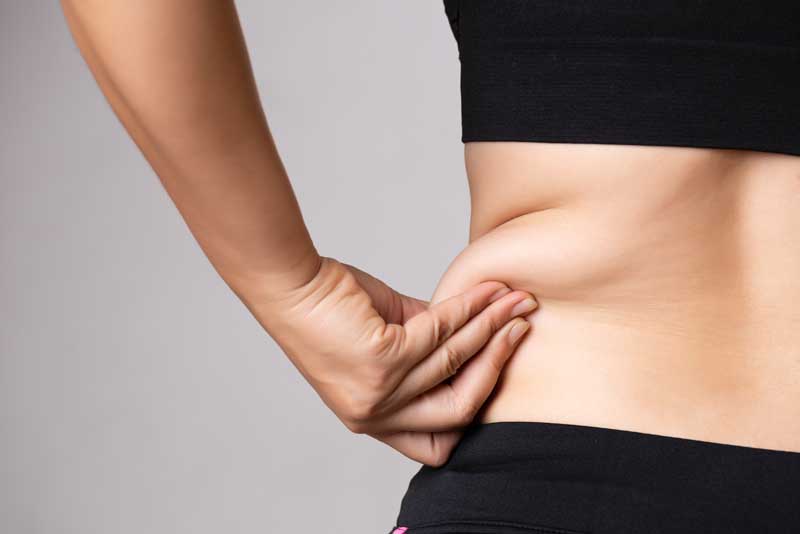 Fat woman hand holding excessive belly fat. Healthcare and woman diet lifestyle concept to reduce belly and shape up healthy stomach muscle. Woman hand holding excessive belly fat.